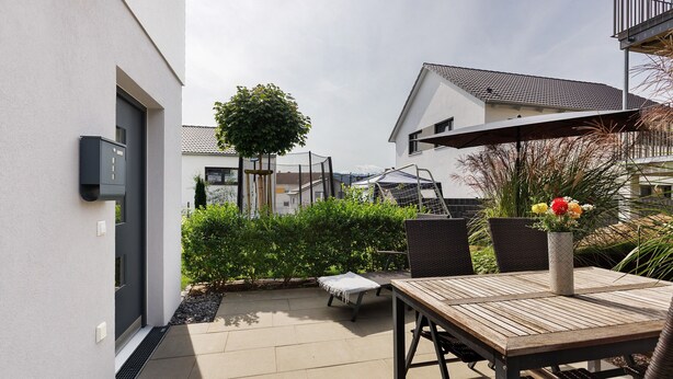 A patio area with a table, chairs, a small garden, and a building in the background. - Apartment 'Seeglück' with Mountain View, Private Terrace and Wi-Fi (Bodman-Ludwigshafen)