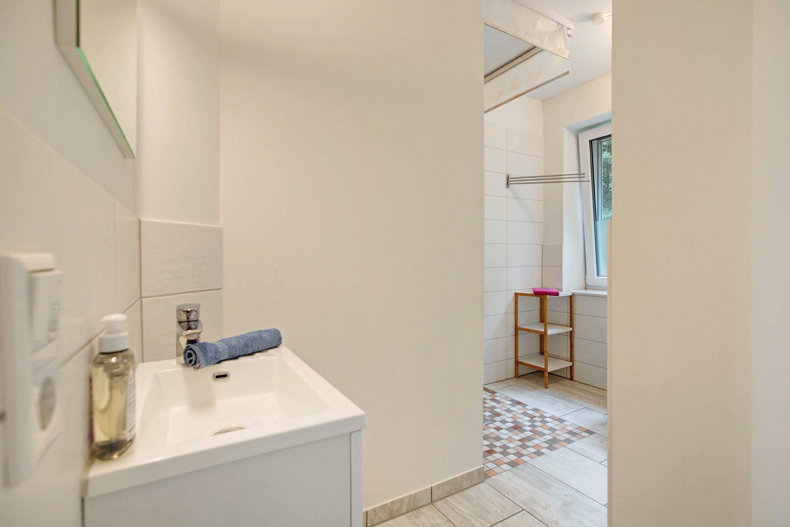 Ein Badezimmer mit einem weißen Waschbecken, einem Spiegel, einem Handtuch und einem Regal mit einem pinkfarbenen Gegenstand.