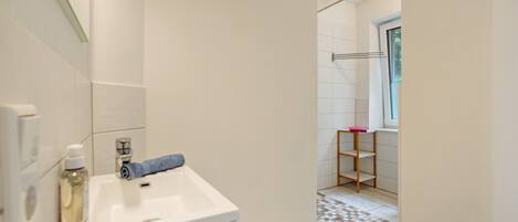 Ein Badezimmer mit einem weißen Waschbecken, einem Spiegel, einem Handtuch und einem Regal mit einem pinkfarbenen Gegenstand.