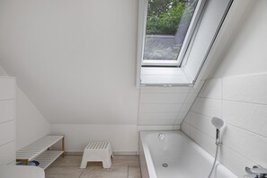 Une petite salle de bain moderne, dotée d’un puits de lumière, d’une baignoire, d’une douche et d’un petit marchepied.