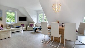 Ein modernes Wohnzimmer mit Essbereich, großen Fenstern und einem Flachbildfernseher.