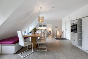 Un appartement moderne de style « loft » comprenant un coin repas, une cuisine et un lit mezzanine servant de chambre.