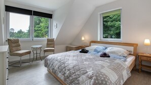 Ein Schlafzimmer mit einem Bett, zwei Stühlen, einem kleinen Tisch und einem Nachttisch mit Lampe.