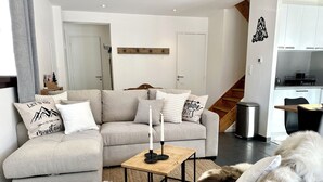 Un salon moderne avec un canapé d’angle gris, une table basse en bois et un chien blanc et duveteux.