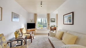 A living room with a sofa, chairs, a TV, and a window with curtains.