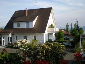 Une maison à deux étages, dotée d’un toit en pente, d’une cheminée bien visible et d’un balcon à l’étage supérieur.