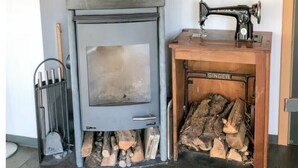 Ein Kaminofen mit Schornstein, eine alte Singer-Nähmaschine und ein Holzstoß.