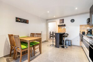 Une cuisine moderne avec un coin repas, comprenant une table et des chaises en bois, un tabouret de bar et une horloge murale.