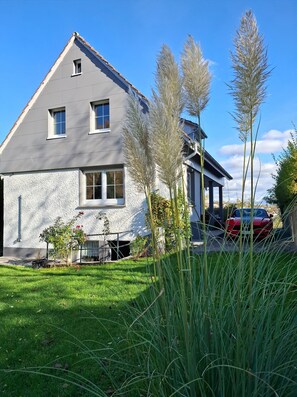 Et moderne hus med skråt tag, et lille vindue og en garage med en rød bil parkeret indeni.