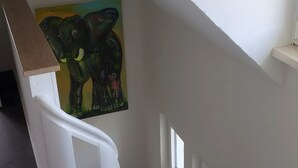 Un escalier avec des rampes blanches, une main courante en bois et un tableau représentant des éléphants sur le mur.