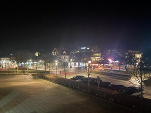 Vista nocturna de una zona comercial con edificios, farolas y coches aparcados.