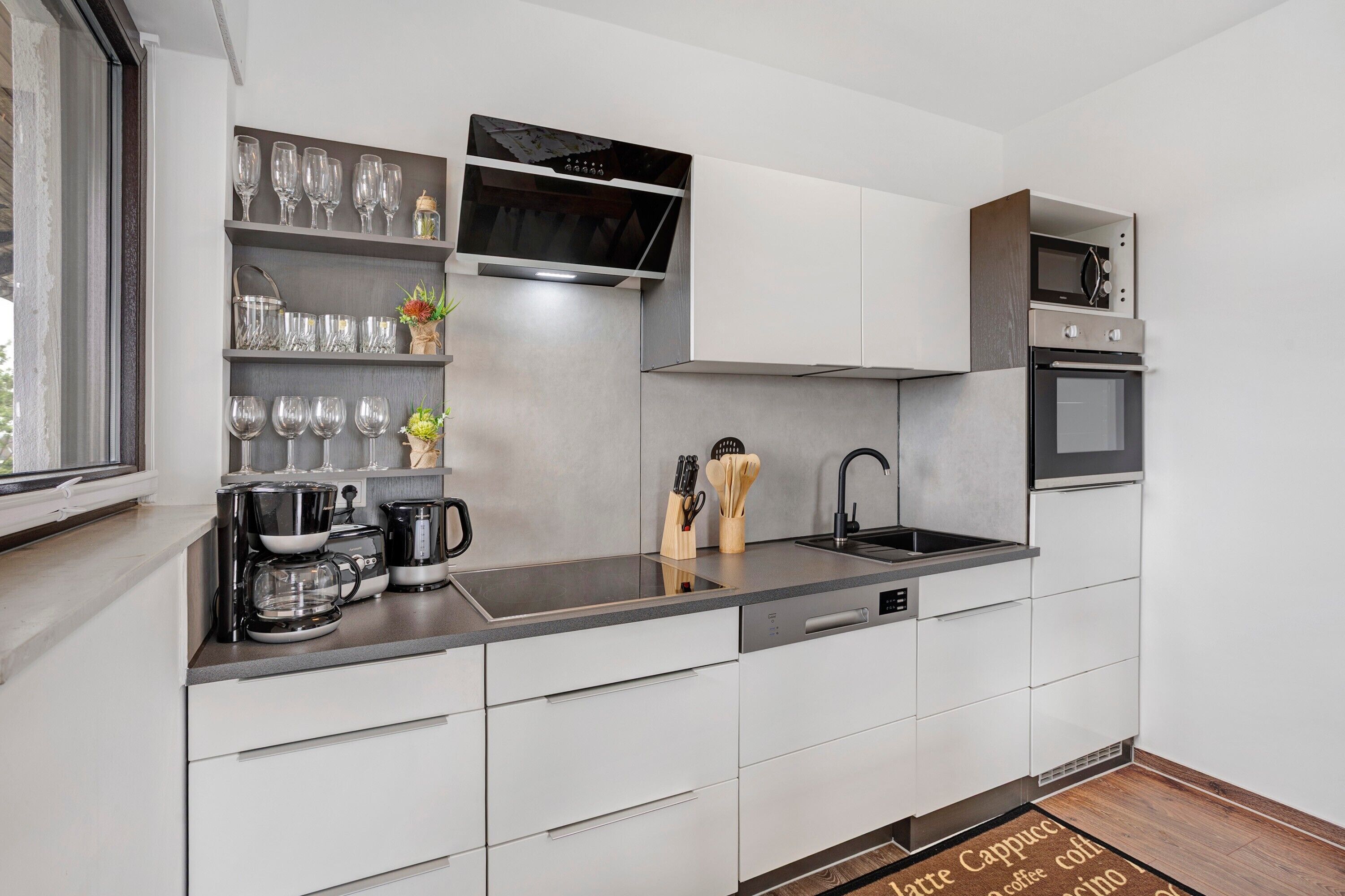 Een moderne keuken met witte kastjes, een roestvrijstalen aanrecht, een koffiezetapparaat en een magnetron.