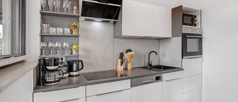 Een moderne keuken met witte kastjes, een roestvrijstalen aanrecht, een koffiezetapparaat en een magnetron.