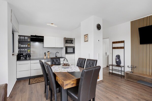 Una cocina moderna con armarios blancos, microondas y cafetera. Hay una mesa de comedor con sillas y un reloj en la pared.