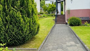 Un chemin menant à un bâtiment doté d’un porche, entouré de verdure et d’une pelouse bien entretenue.