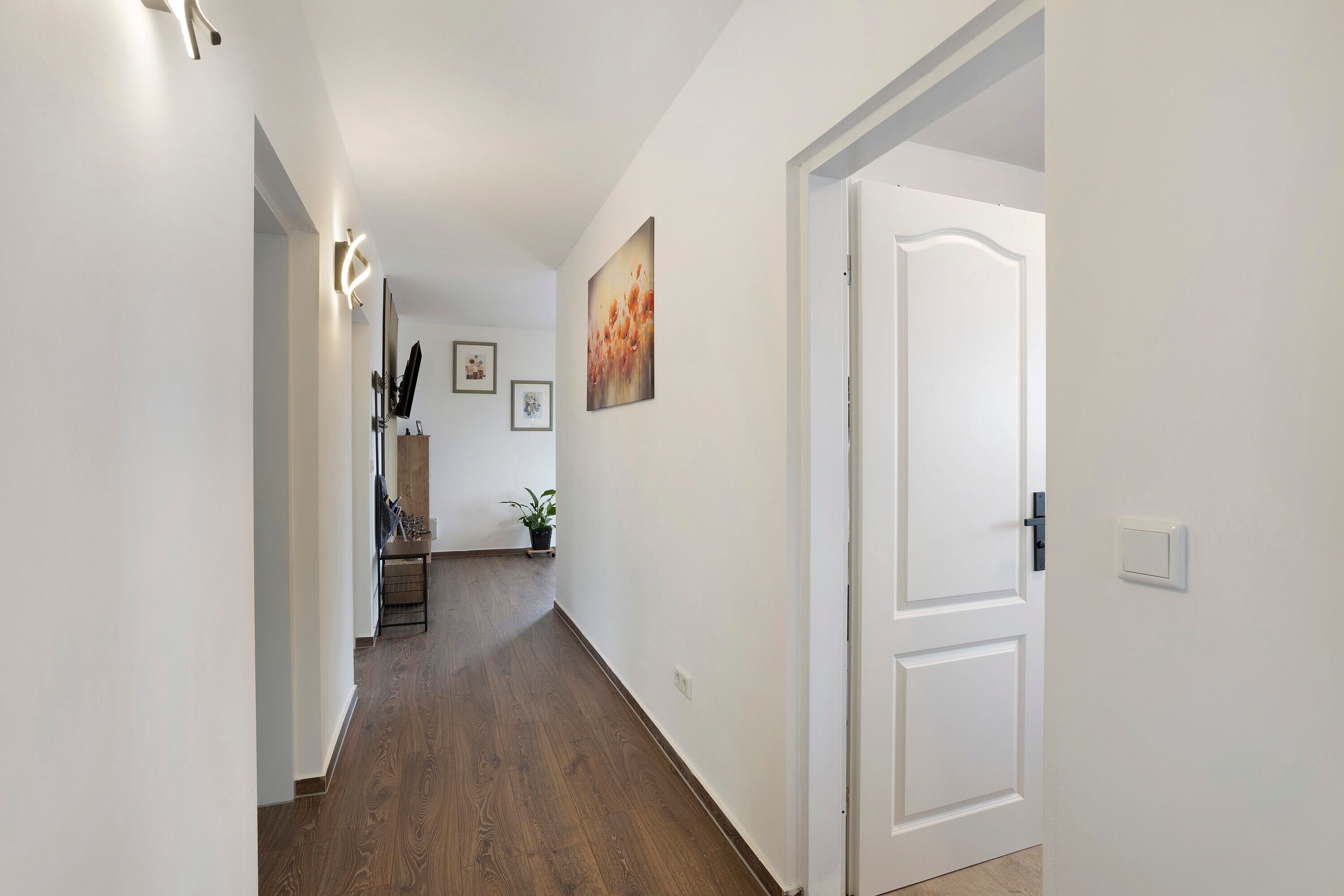Ein Flur mit Holzboden, weißen Wänden, einer Tür und einem gerahmten Bild an der Wand.