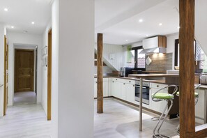 Une cuisine moderne avec des meubles blancs, un pilier décoratif en bois et un tabouret de bar vert.