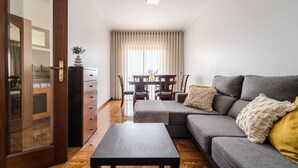 A modern living room with a grey sofa, a wooden coffee table, and a dining area with a table and chairs.