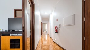 A hotel hallway with a wooden floor, a reception desk, a fire extinguisher, and a door at the end.