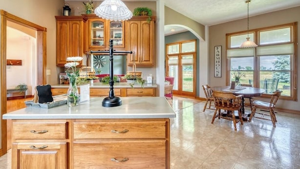 A spacious kitchen with wooden cabinets, a central island, and a dining area with wooden chairs. - Charming Rural Farmhouse on a Working Alpaca Farm (Flora)