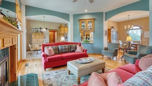A spacious living room with a red sofa, a grey ottoman, and a blue armchair. There is a wooden cabinet and a chandelier. - Charming Rural Farmhouse on a Working Alpaca Farm (Flora)