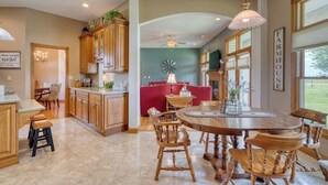 A spacious kitchen with wooden cabinets, a dining table with chairs, and a red sofa in the background. - Charming Rural Farmhouse on a Working Alpaca Farm (Flora)