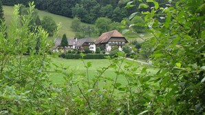 Un bâtiment traditionnel doté d’un toit en pente, entouré d’une végétation luxuriante et adossé à une colline boisée.
