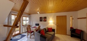Una stanza con soffitto in legno, un tavolo da pranzo con sedie, un divano, una porta e una finestra.