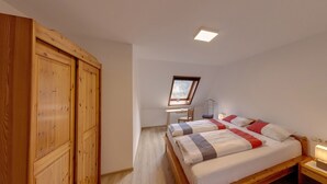 A bedroom with two beds, a wooden wardrobe, a desk with a chair, a window, and a bedside table with a lamp. - Apartment 'Pfauensitz' with Mountain View, Shared Garden and Wi-Fi (Seelbach)