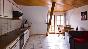 A kitchen with wooden cabinets, a stove, and a dining area with a table and chairs. - Apartment 'Pfauensitz' with Mountain View, Shared Garden and Wi-Fi (Seelbach)
