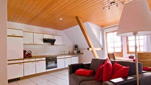 A modern kitchen with white cabinets, a microwave, and a stove. There is a gray sofa with red cushions and a lamp in the foreground. - Apartment 'Pfauensitz' with Mountain View, Shared Garden and Wi-Fi (Seelbach)
