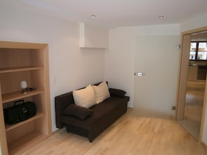 A room with a brown sofa, a wooden shelf with a lamp and a bag, and a door leading to a kitchen area. - Apartment 'Rossblick, 60qm' with Mountain View, Shared Garden and Wi-Fi (Seelbach)