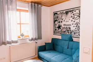Une pièce avec un canapé bleu, un radiateur, une fenêtre avec des rideaux et un mur orné d’une affiche.