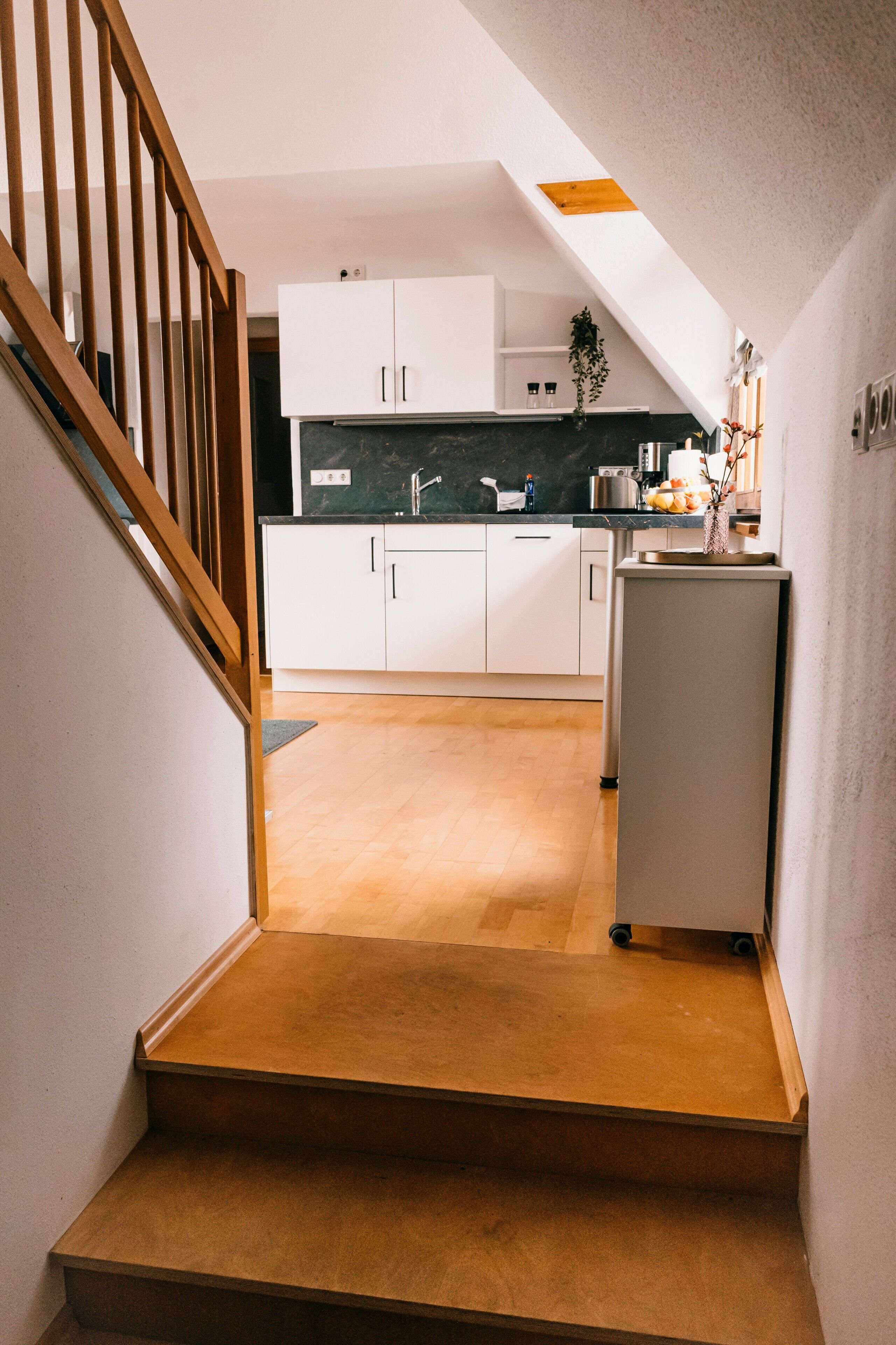 A kitchen with white cabinets, a wooden staircase, and a small refrigerator.