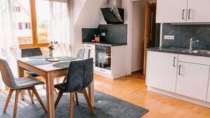 A modern kitchen with a built-in oven, a dining area with a table and chairs, and a view of the outside. - Holiday Apartment 'Alte Schneiderei' with Balcony and Wi-Fi (Heideck)