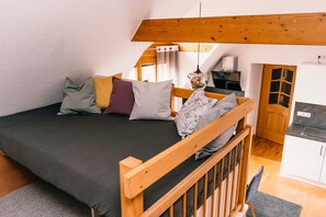 Une chambre à coucher comprenant un lit, des oreillers, une tête de lit en bois, un bureau et un coin cuisine.