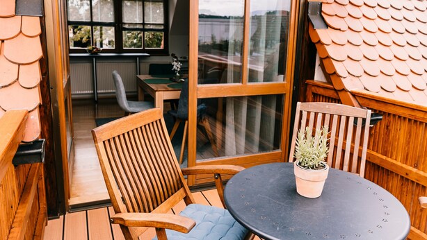 A wooden deck with a table and chairs, a potted plant, and a view through a glass door. - Holiday Apartment 'Alte Schneiderei' with Balcony and Wi-Fi (Heideck)