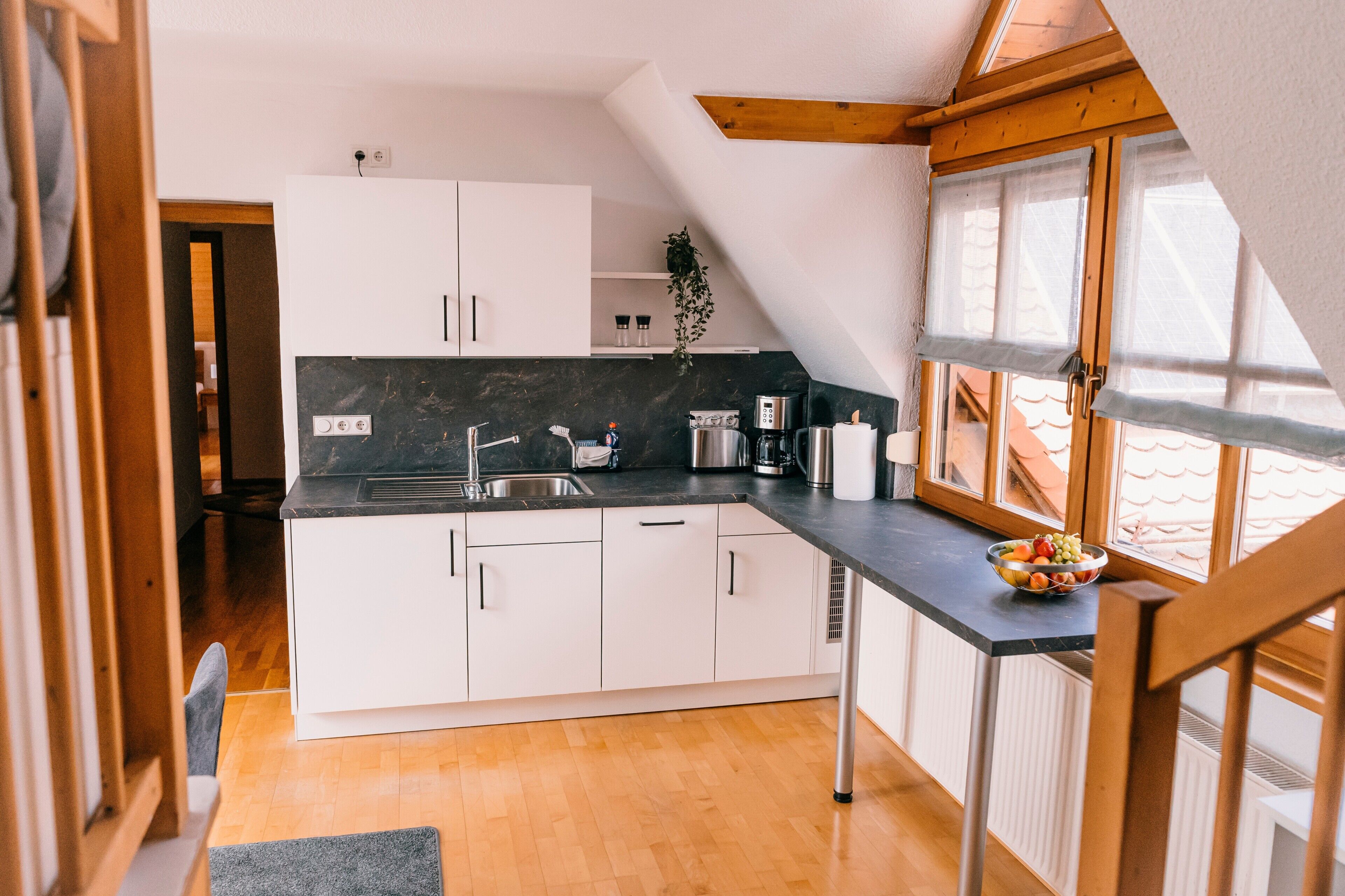 Une cuisine moderne avec des meubles blancs, un plan de travail noir et une fenêtre donnant sur le toit.