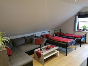 Une chambre de style loft avec un canapé, deux lits simples, une petite table avec une bougie et une fenêtre agrémentée de plantes.