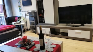 A living room with a TV, a cabinet, a table with a bottle and glasses, and a chair. - Apartment 'Schöner' with Balcony and Wi-Fi (Oberharmersbach)
