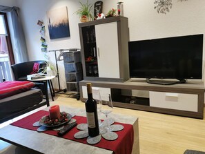 A living room with a TV, a cabinet, a table with a bottle and glasses, and a chair.