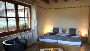 A bedroom with a bed, bedside tables, a chair, a radiator, a window with curtains, and a view of the outside. - Apartment 'Sonnenschein, 80qm' with Mountain View, Shared Garden and Wi-Fi (Seelbach)