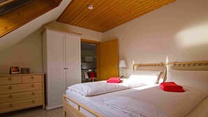 Ein Schlafzimmer mit Holzboden, einem Bett mit weißer Bettwäsche, einem hölzernen Schminktisch und einem Kleiderschrank.