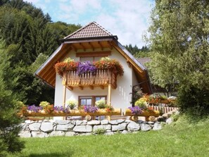 Een chalet met balkon, stenen fundering en weelderige begroeiing.