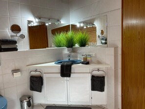 Un baño con un tocador blanco, un espejo redondo, un lavabo azul y una planta en maceta.