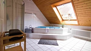 Ein Badezimmer mit einer Badewanne, einer Dusche, einer hölzernen Sitzbank und einem Oberlicht.