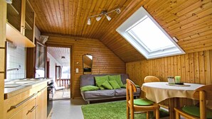 Un interno in legno con cucina, zona pranzo e camera soppalcata con finestra a lucernario.
