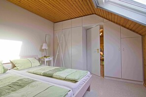 A bedroom with two beds, a wooden ceiling, and a wardrobe.