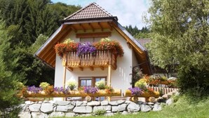 Eine Chalet mit Balkon, Stein Fundament und üppiger Bepflanzung.