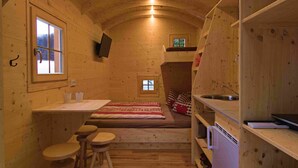Eine kleine Holz-Blockhütte mit Kochnische, kleinem Fenster und einem Bett.